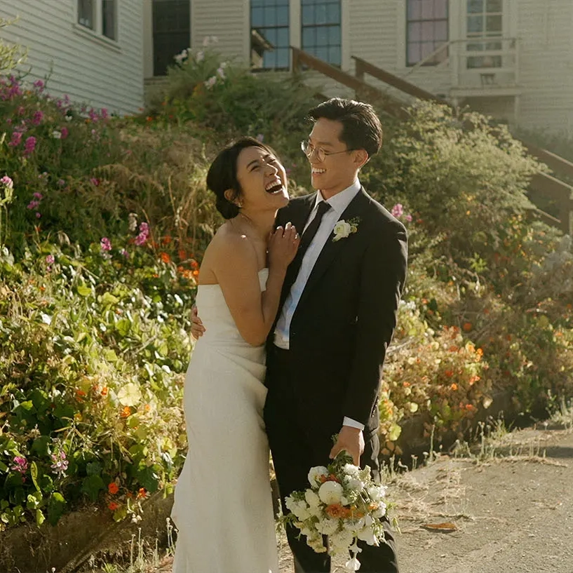 Bride and groom laughing together in a flower-filled garden.